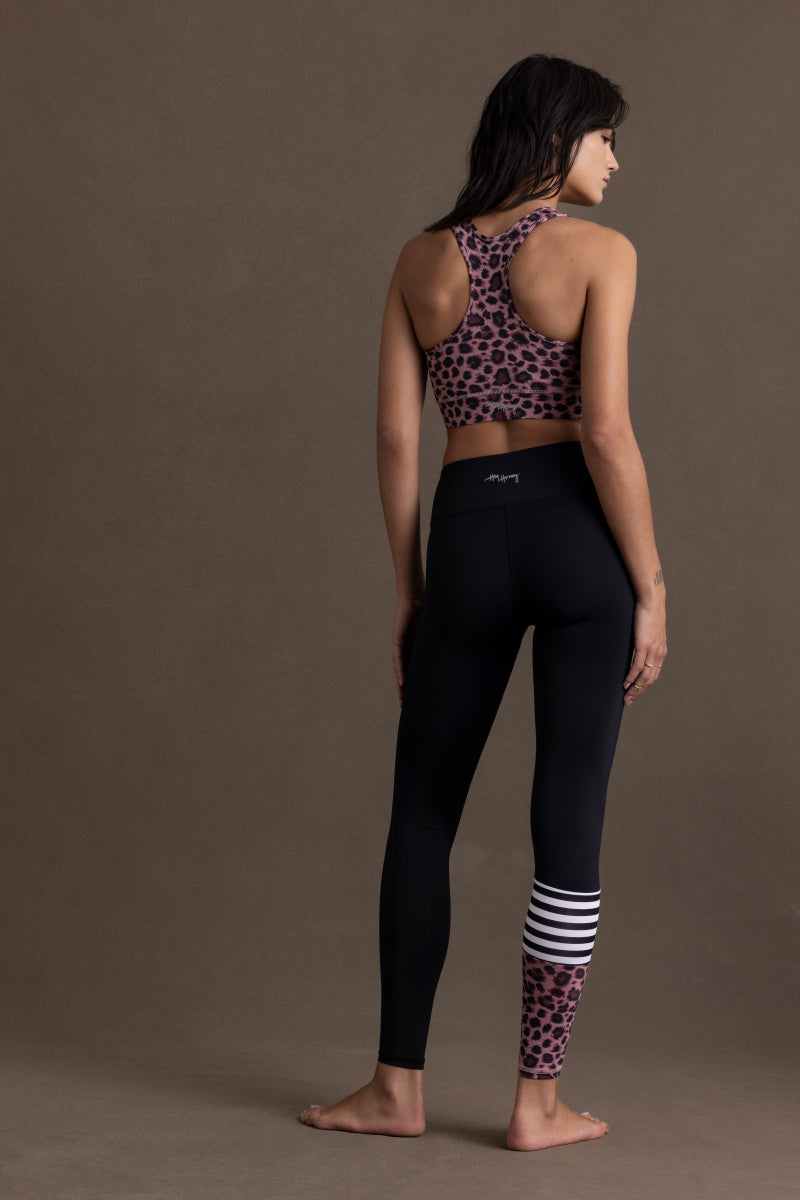 Woman in leopard print sports bra and black leggings, showcasing trendy surf style and comfort for yoga and fitness.