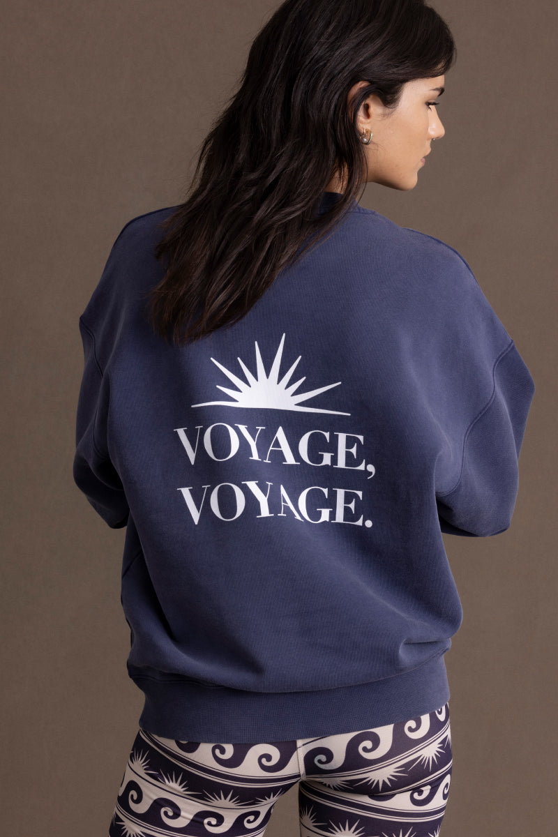 Woman wearing a navy sweater with 'Voyage, Voyage' print and a sun design, paired with patterned leggings.