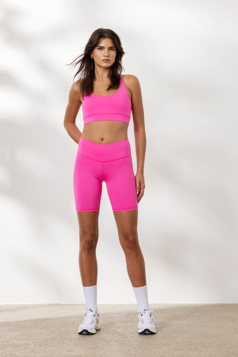 Model wearing Hey Honey Yoga Biker Neon Pink set, showcasing a flattering high waist and vibrant neon color for active wear.