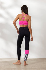 Woman in neon pink surf style yoga set with back straps, showing high-waisted leggings and sporty design.
