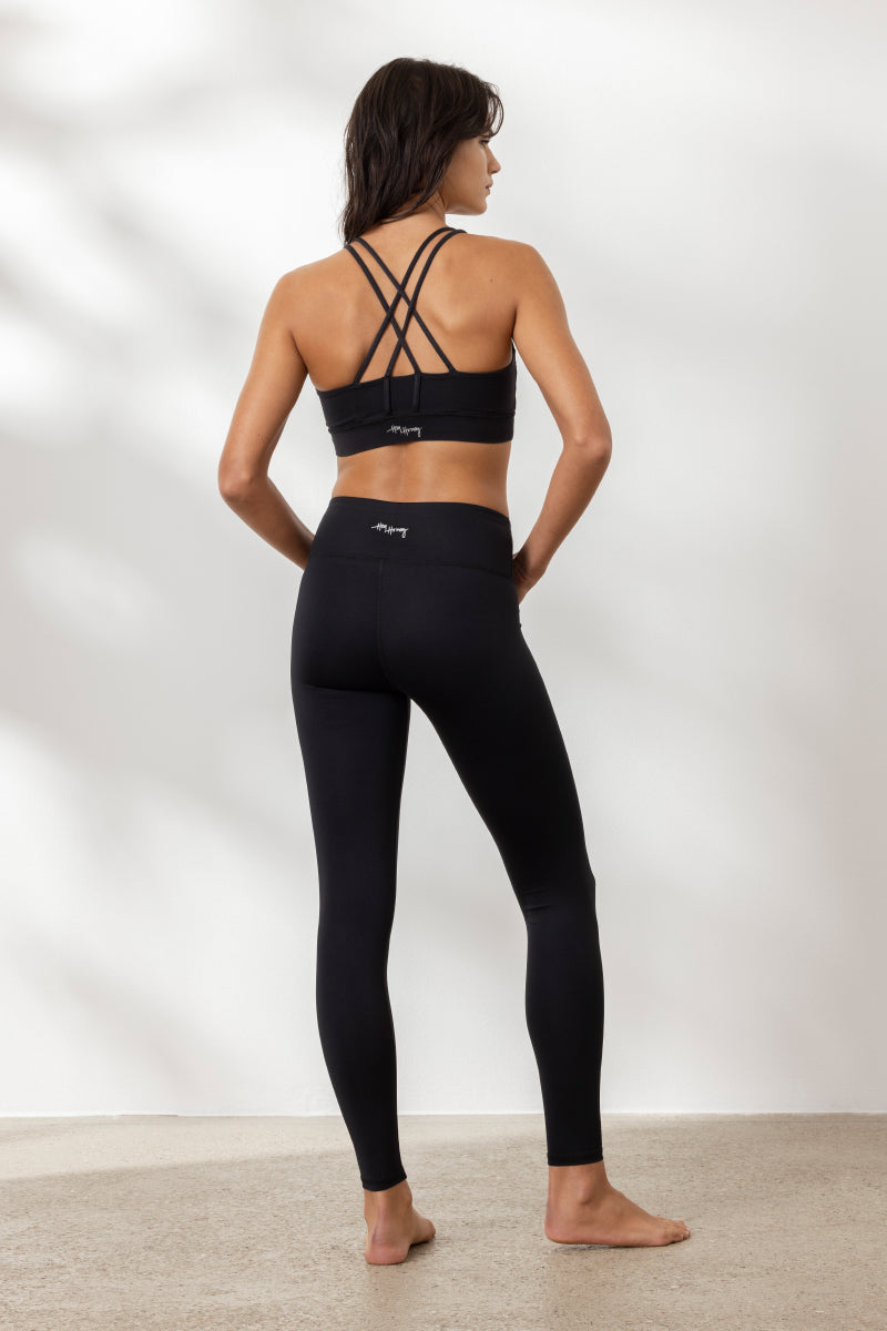 Woman wearing Hey Honey Black Leggings and a strappy black sports bra, showcasing a stylish yoga outfit from the back.