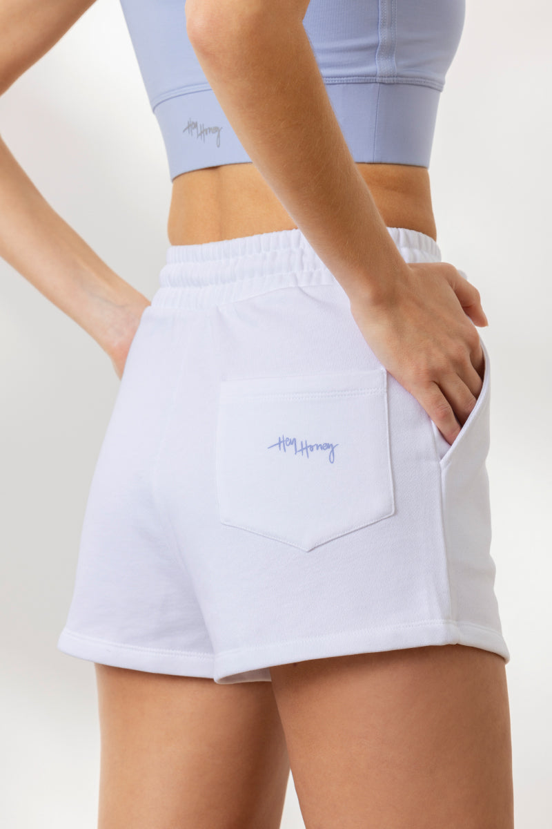 Model showcasing white sweatshorts with "Hey Honey" logo, featuring a comfortable elastic waistband and pockets.