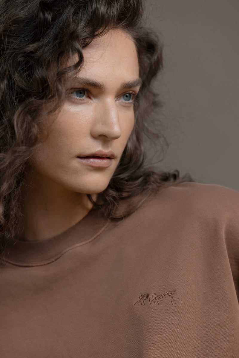 Model wearing relaxed fit Trui Cacao sweater, showcasing soft cotton fabric in a warm brown tone.