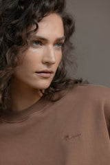 Model wearing relaxed fit Trui Cacao sweater, showcasing soft cotton fabric in a warm brown tone.