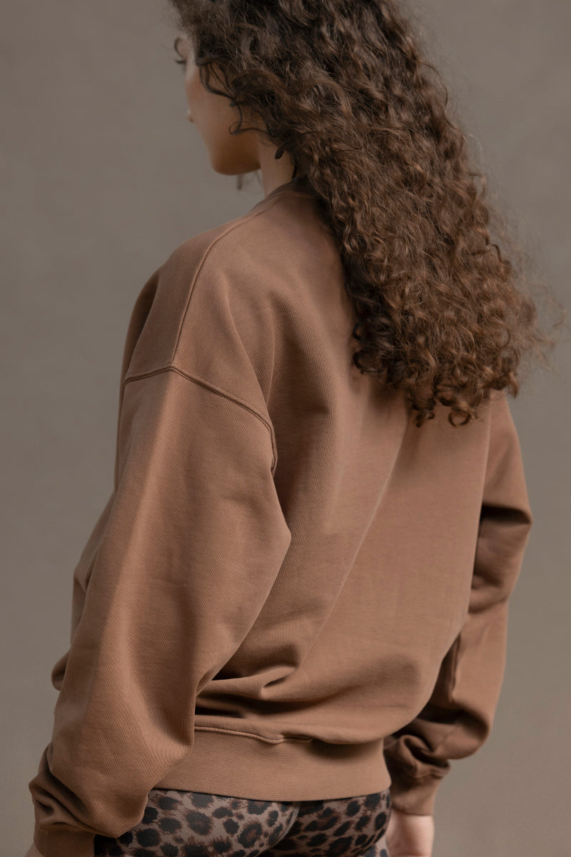 Model showcasing the Trui Cacao sweater, a cozy brown cotton pullover with a relaxed fit, perfect for casual wear.
