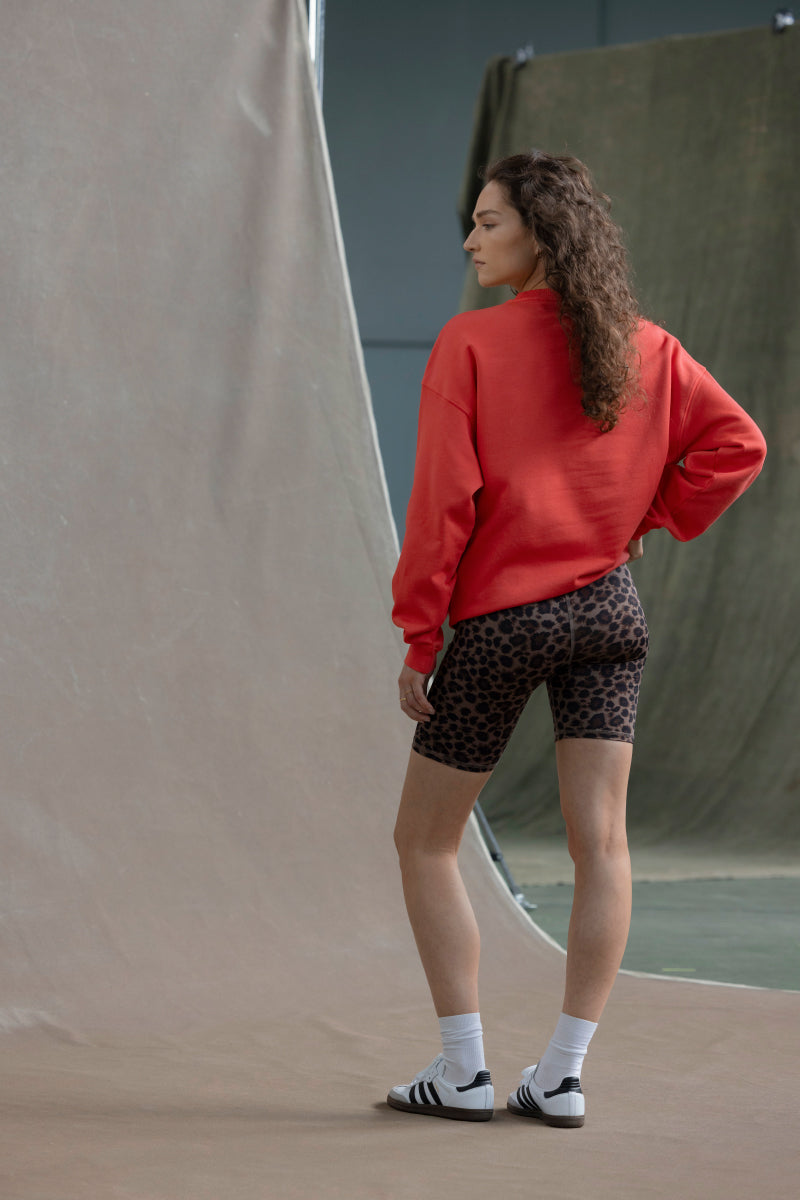 Model wearing a red sweatshirt and leopard print shorts, showcasing a relaxed outfit against a neutral backdrop.