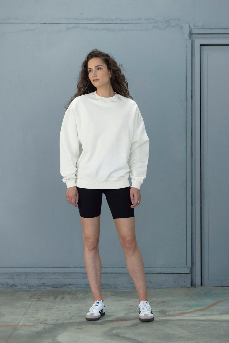 Model wearing Trui Voyage Off-White sweater with black shorts, showcasing a relaxed and stylish look.