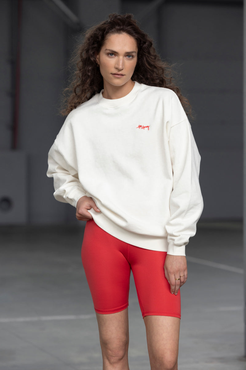 Model wearing a white oversized sweatshirt paired with red cycling shorts, showcasing a relaxed athletic look.