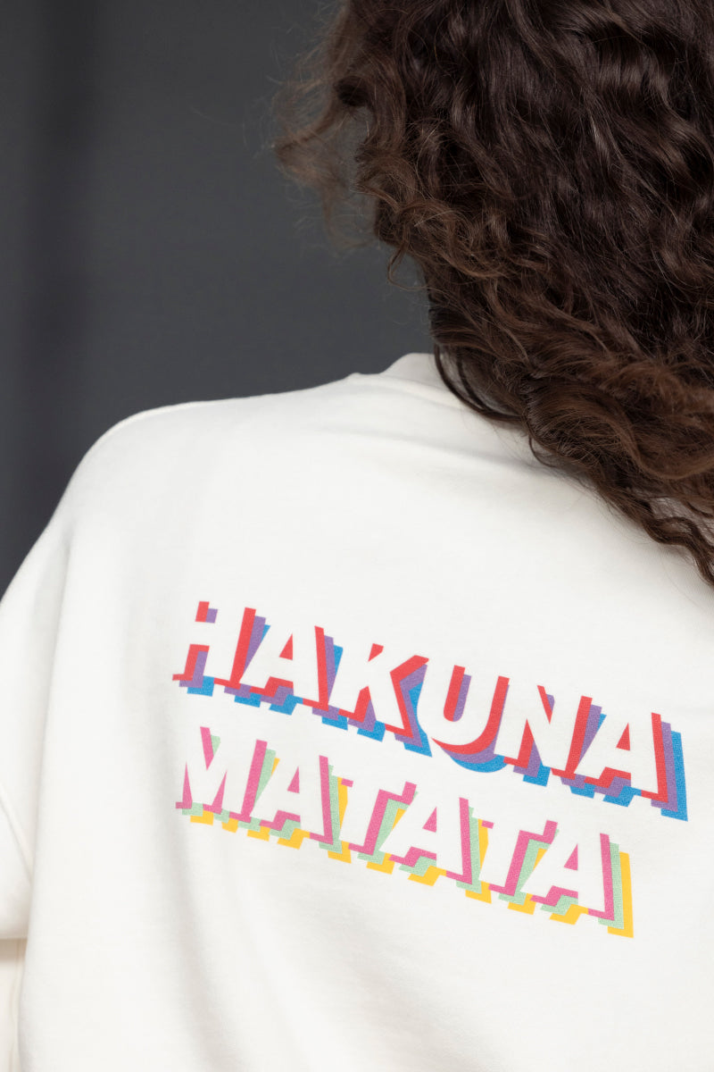 Rear view of cream sweater featuring colorful "Hakuna Matata" graphic, showcasing relaxed fit and soft cotton material.
