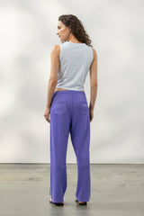 Woman wearing a light grey sleeveless top and purple pants, showcasing a casual and comfortable style from the back.