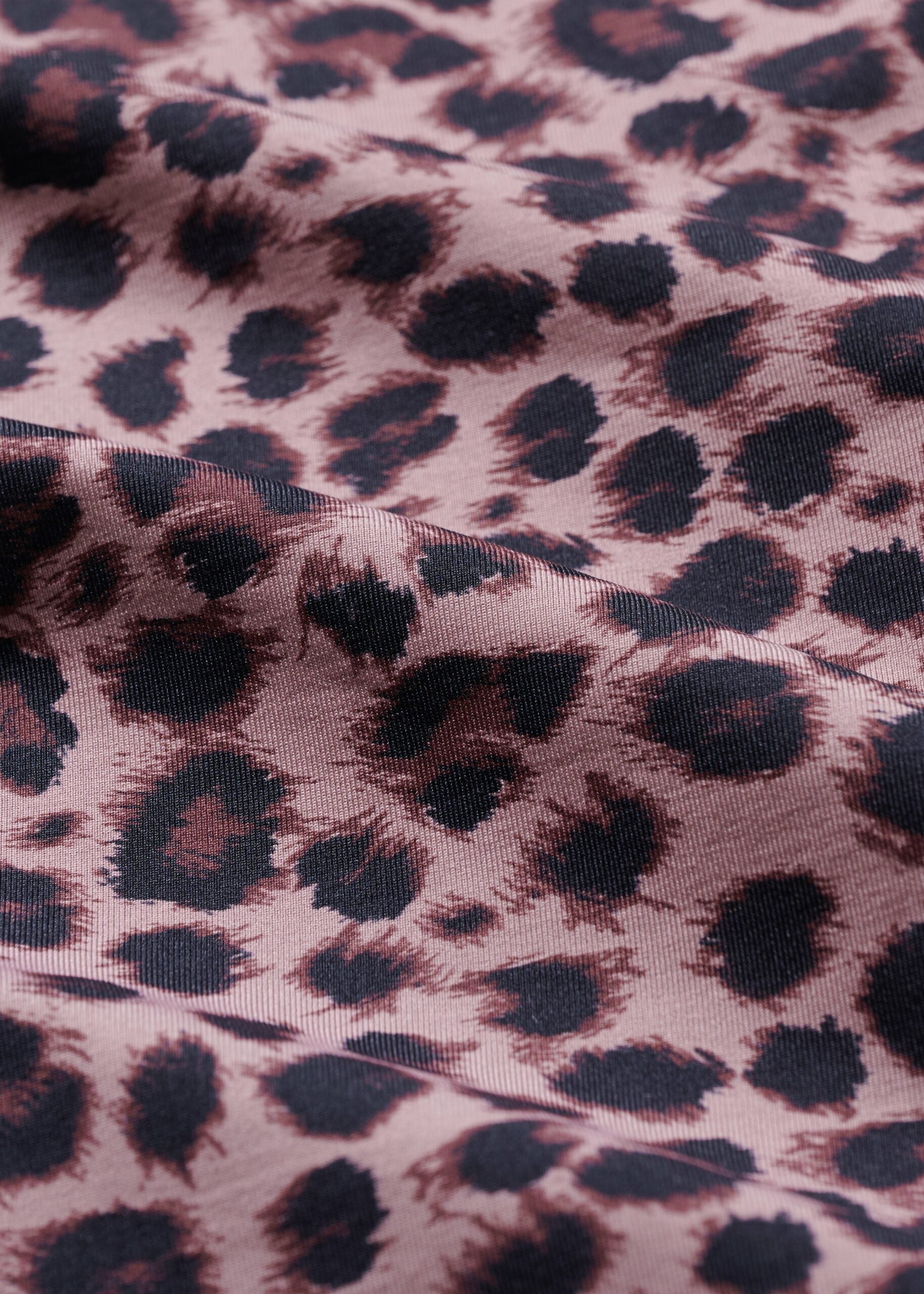 Close-up of soft pink leopard print fabric featuring dark spots, ideal for stylish yoga and fitness wear.