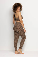 Woman with curly hair wearing leopard print leggings and matching top, showcasing a stylish yoga outfit.