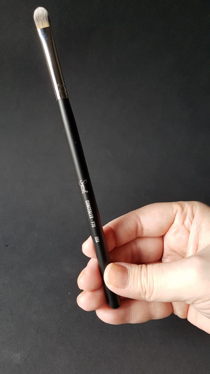 Sigma F70 concealer brush held in hand, showcasing its precise design and high-quality construction for flawless application.