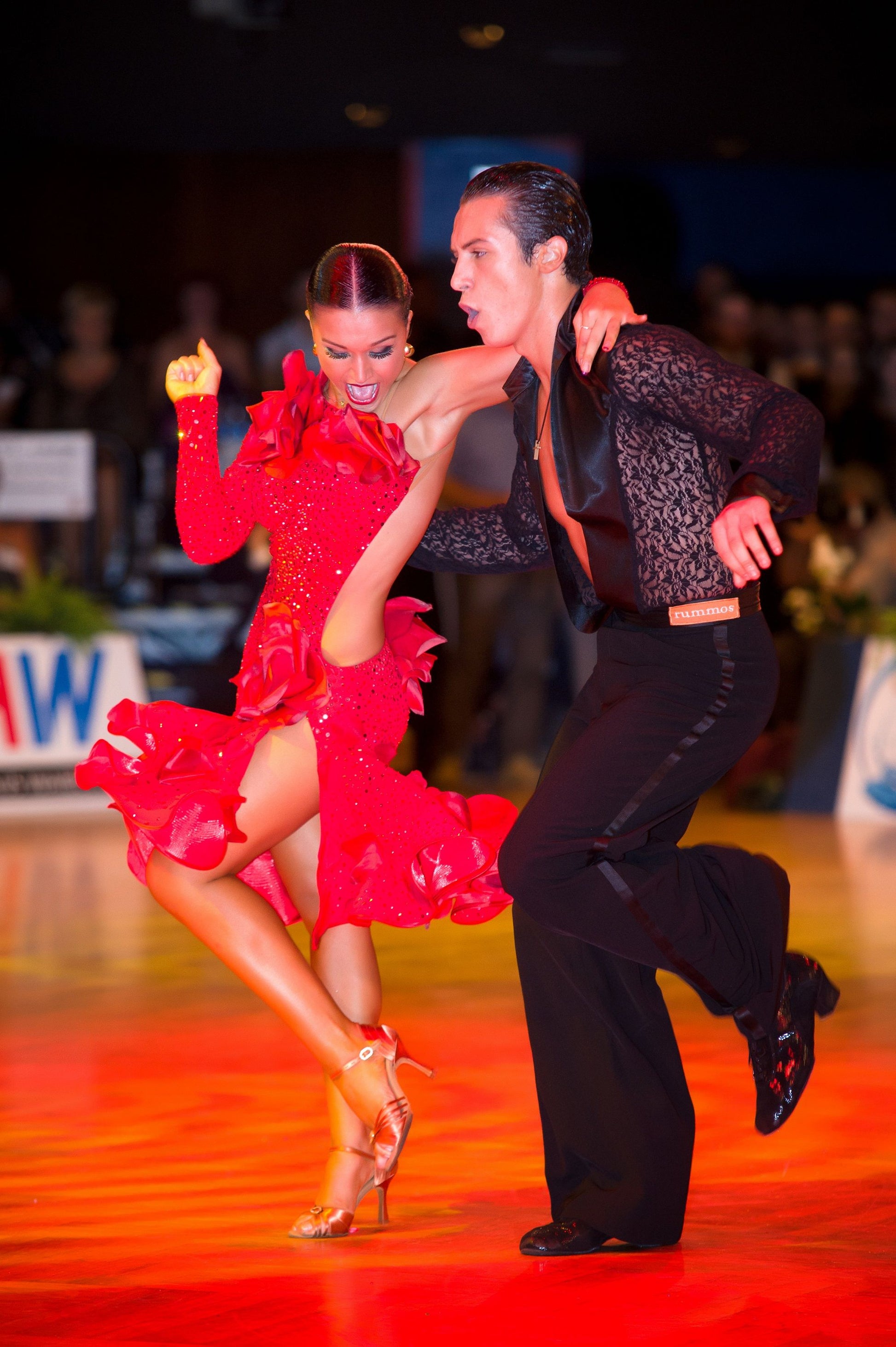 Elegant couple performing a lively dance in red costumes at a ballroom competition, showcasing their passion and skill.