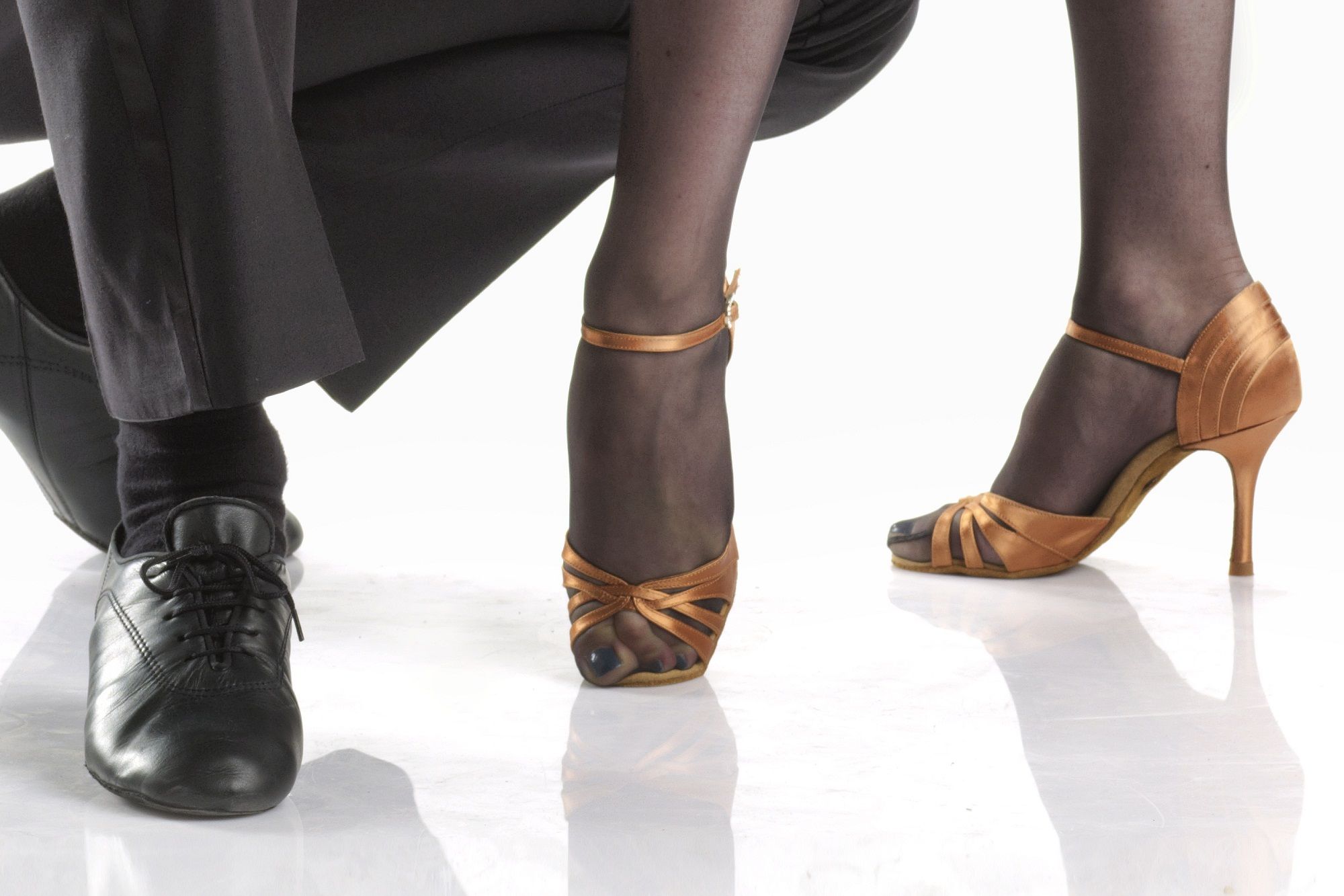 Elegant dance shoes for performers, showcasing a black leather shoe and a stylish orange sandal on a reflective surface.